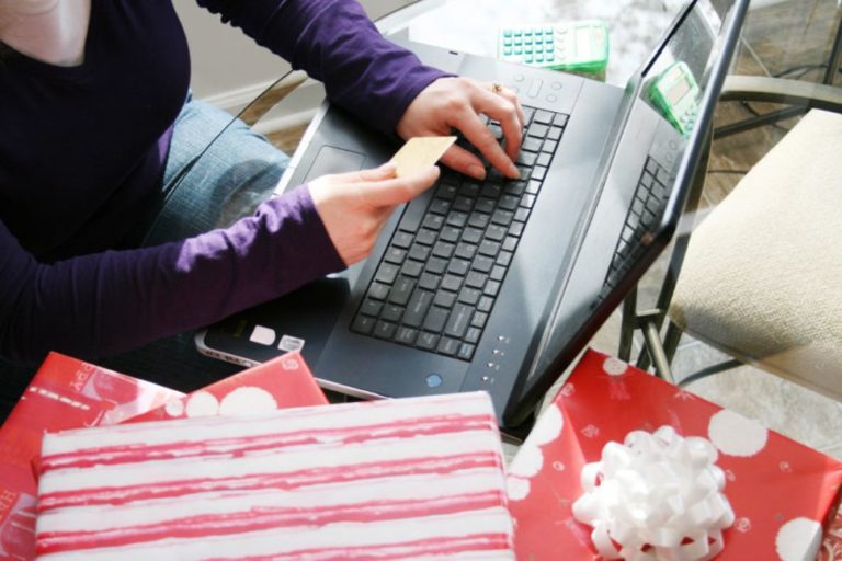 A woman holding a credit card shopping on her laptop during cyber monday surrounded by holiday gifts and other purchases